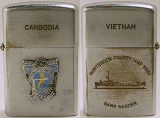 Vulcan brand lighter marked "Cambodia" and an attached badge for USS Hunterdon County Game Warden.&nbsp; The back reads"Vietnam - AGP 838 USS Hunterdon County Game Warden" and has a line drawing of the ship